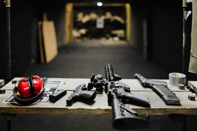 Gun store setup featuring firearms, safety gear, and accessories on a table in a shooting range environment.