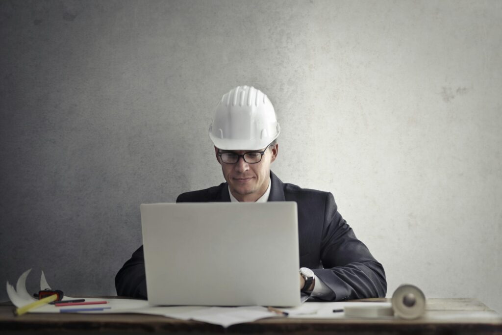 Construction professional in a hard hat using a laptop to prepare a project proposal