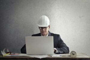Construction professional in a hard hat using a laptop to prepare a project proposal