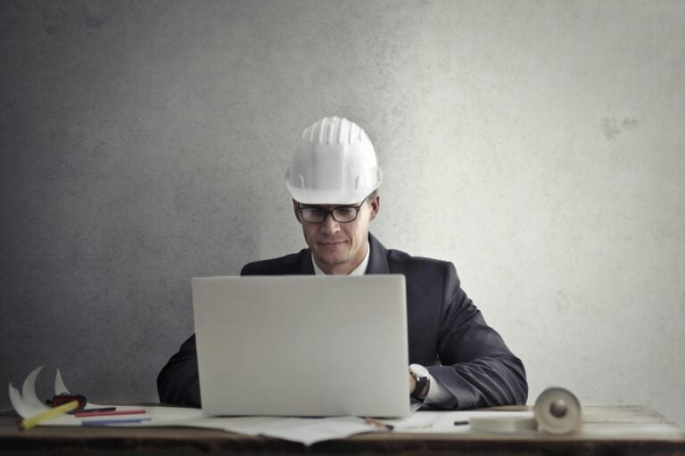 Construction professional in a hard hat using a laptop to prepare a project proposal